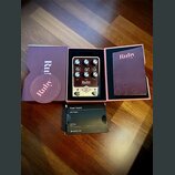 Kytarový pedál v barvě stříbrné a černé, umístěný v originální fialové krabici. Na pedálu je nápis Ruby, TOP BOOST AMPLIFIER '63 a logo UA v kosočtve…