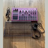 Fialový sampler s nápisy electribe sampler a KORG. Zařízení obsahuje displej, několik otočných knoflíků a mřížku s čtvercovými padovými tlačítky. K p…