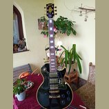 Černá elektrická kytara typu Les Paul se zlatým hardwarem a bílými vložkami na hmatníku. Na hlavě je nápis Gibson a logo s hvězdou, na hmatníku je u…