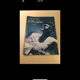 Fotografie znázorňuje obal CD nebo album s portrétem muže v brýlích a bílém saku. V horní části je nápis „the very best of Elton John“. Předmět leží…