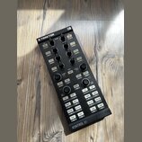 Černý DJ kontrolér s nápisy TRAKTOR a KONTROL X1. Zařízení obsahuje několik řad knofíků, posuvníků a bílých tlačítek s popisky jako DELAY, REVERB, FI…
