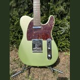 Elektrická kytara typu Telecaster v olivově zelené metalické barvě s hnědo-červeným vzorovaným pickguardem. Nástroj má javorový hmatník a chromované…