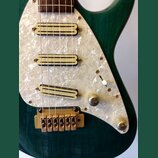 Detail elektrické kytary s tmavě zeleným povrchem a bílým perleťovým pickguardem. Nástroj má tři humbuckerové snímače s krémovými kryty, přičemž na s…