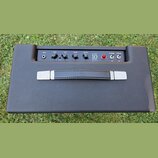 Kytarový kombozesilovač v černém texturovaném potahu s černým ovládacím panelem. Na panelu jsou nápisy INPUT, GAIN, TONE, REVERB, MASTER, STUDIO 10 E…