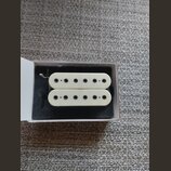 Dvě bílé humbucker snímače s šesti viditelnými póly umístěné v bílé krabičce na černém polstrování. Na snímačích nejsou žádné viditelné značky, loga…