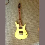 Žlutá elektrická kytara s tmavým hnedým hmatníkem a černou hlavou. Na hlavě je viditelné logo značky Ibanez. Nástroj má dva černá humbuckery, jeden o…