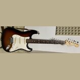 Elektrická kytara typu Stratocaster s barevným přechodem korpusu od černé přes hnědou k žluté. Má bílý pickguard, tři snímače a hnědý hmatník. Na hla…