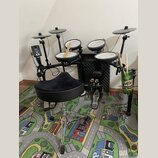 Elektronická bicí souprava s černým rámem a pět verifyingmi padů. Na modulu je nápis Roland, na pedálech značka Roland. Součástí je černý polstrovaný…