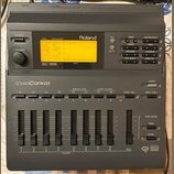 Šedý digitální modul Roland SC-155 Sound Canvas. Zařízení má podsvícený displej s textem „01 001 Piano 1“, řadu tlačítek a osm posuvníků s označením…
