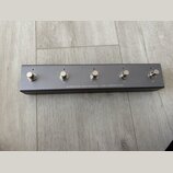 Šedý MIDI footswitch v kovovém obalu s pěti stříbrnými spínači. Na spodní hraně je bílý nápis DARKGLASS ELECTRONICS - MIDI FOOTSWITCH. Povrch zařízen…