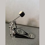 Stříbrný basový pedál s černým šlapadlem. Na šlapadle jsou nápisy IRON COBRA 200 a logo TAMA. Povrch vykazuje mírné známky používání v podobě drobnýc…