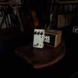 Bílý efekt pedál s nápisem FUZZ a logem JHS SERIES. Na horní straně jsou tři ovládací knoflíky s popisky VOLUME, BASS a FUZZ. Vedle pedálu je umístěn…