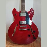 Červená polodubová elektrická kytara s hnědým hmatníkem. Nástroj má dva humbuckery s chromovanými kryty, chromovaný most a stopku. Na těle jsou čtyři…