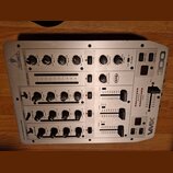 Stříbrný DJ mixér s nápisy BEHRINGER a VMX 100. Na horní části jsou ovládací prvky pro MAIN OUT, OUT A a OUT B, vpravo je vidět logo XPO. Přístroj ob…