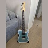 Elektrická kytara s modrým přechodovým povrchem těla a hnědým hmatníkem. Na hlavě je viditelné logo Fender. Hmatník obsahuje bílé dekorativní vložky…
