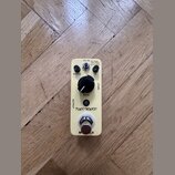 Krémový efekt pedál s nápisy FUNKY MONKEY a MOOG. Na horní straně jsou ovládací prvky: dva malé černé knoflíky u nápisů RANGE a Q, jeden velký černý…