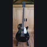 Černá elektrická kytara s tmavým hmatníkem a bílým trsátorem. Na hlavě i na trsátoru je bílý nápis GRETSCH. Nástroj má dva snímače typu humbucker a j…