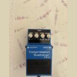 Modrý efekt pedál s černým spínacím tlačítkem. Na horní části jsou čtyři bílé ovládací knoflíky s popisky LEVEL, TONE, ATTACK a SUSTAIN a červená kon…