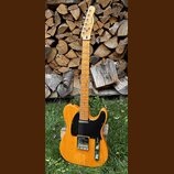 Elektrická kytara s přírodním dřevěným povrchem těla a hmatníku. Na hlavě je viditelné logo Fender. Kytara má černý pickguard a dva snímače. Povrch t…