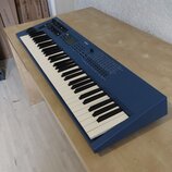 Modrý elektronický klávesový nástroj s bílými a černými klávesami. Na horním panelu je viditelné logo ROHM, displej a řada ovládacích tlačítek a posu…