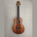 Hnědý dřevěný ukulele s tmavým hmatníkem a černými ladičkami. Uvnitř ozvučnice je vidět štítek s nápisem "KALA". Na hlavě nástroje je bílý nápis "KAL…