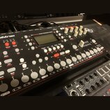 Šedý sampler s nápisy Elektron a OCTATRACK. Na horní části je displej a text DYNAMIC PERFORMANCE SAMPLER. Zařízení obsahuje bílé ovratové tlačítka, č…