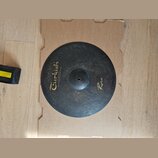 Kruhový činely z tmavého kovaného kovu s viditelnou strukturou kladivování. Na povrchu je žlutý nápis „Turkish“ a pod ním menší text „Handmade cymbal…
