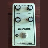 Bílý kytarový efekt s nápisem RC-BOOSTER a logem m.electronics v dolní části. Pedál má čtyři černé ovládací knoflíky s popisky VOLUME, GAIN, TREBLE a…
