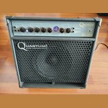 Černý basový kombozesilovač s kovovou mřížkou reproduktoru. Na předním panelu je nápis HUGHES & KETTNER QUANTUM BASS TECHNOLOGY a označení modelu QC…