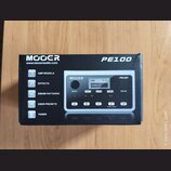 Fotografie znázorňuje kartonovou krabici s produktem Mooer PE100. Na krabici jsou nápisy MOOER, www.mooeraudio.com a modelové označení PE100. Jsou zd…