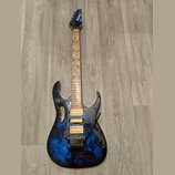 Elektrická kytara s modře a černě strakatým povrchem korpusu a hnědým hmatníkem s modrými ornamenty listů. Na hlavě je bílý nápis Ibanez. Nástroj má…