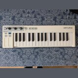 Bílá klaviatura s 32 klávesami. Na horním panelu je vpravo nápis ARTURIA a pod ním text YOUR EXPERIENCE YOUR SOUND, vlevo nápis KEYSTEP. Přístroj obs…