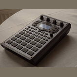 Černý sampler s množstvím gumových padů, tlačítek a ovládacích knoflíků. Na horní hraně je nápis Novation GrooveStation II. Zařízení obsahuje malý di…
