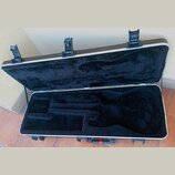 Otevřený tvrdý kufýr na elektrickou kytaru s černým plyšovým vnitřkem. Kufýr má olivově zelený povrch, bílý lem a tři černé kovové zámky. Na vnitřní…