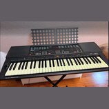 Černý digitální klavír s bílými klávesami a integrovaným notovým stojanem z perforovaného plastu. Na ovládacím panelu je viditelné logo YAMAHA a nápi…