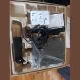 Fotografie znázorňuje otevřenou kartonovou krabici s polystyrenovými vložkami, ve které je umístěno několik komponentů. V krabici se nachází černý hr…