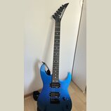 Modře lakovaná elektrická kytara s černým hmatníkem a černými hardwarem. Na hlavě je bílý nápis Jackson. Nástroj má dva humbuckery, jeden ovládací kn…