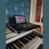Černý sampler MPC s integrovaným dotykovým displejem, na kterém je zobrazeno rozhraní softwaru. Na přední hraně přístroje je bílý nápis MPCX. Zařízen…