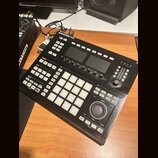 Černý kontrolér Maschine Studio s mřížkou 16 bílých podsvícených padů. Na horní hraně je nápis MASCHINE STUDIO s logem výrobce. Zařízení obsahuje dvě…