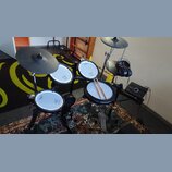 Elektronická bicí souprava značky Roland s bílými padovými plochami a černými činely. Na padech jsou viditelné nápisy Roland a V-Drums. Součástí je č…