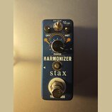 Modrý efekt pedál s nápisy HARMONIZER a stax. Na horní části jsou dva černé otočné knoflíky s popisky DRY a WET, centrální knoflík s rozsahovou stupn…