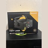 Fotografie znázorňuje kartónové balení laserového efektu. Na krabici je zobrazen černý přístroj s rukojetí a nápisy beamZ, ACRUX a PARTY LASER. V pra…