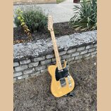 Elektrická kytara typu Telecaster v žlutém provedení s černým pickguardem. Na hlavě hmatníku je viditelné logo Squier. Nástroj vykazuje známky použív…
