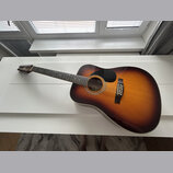 Akustická kytara s korpusem v barevném přechodu od žluté přes oranžovou k hnědé (sunburst). Na hmatníku jsou vidět bílé polohové značky a na hlavě ná…