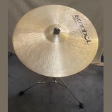 Zlatavý kovový činel umístěný na chromovaném stojanu. Na povrchu je černý nápis „Istanbul“ s hvězdicí a pod ním menší text „Mehmet Handmade Cymbals f…