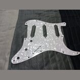 Bílý pickguard s perleťovým efektem určený pro elektrickou kytaru. Povrch je hladký a reflexní, bez viditelných značek, log nebo nápisů. Kousek vykaz…