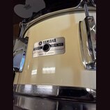 Detail kremple bubnu v krémové barvě s chromovaným obručem a lugy. Na korpusu je kovový štítek s nápisy YAMAHA, MODEL 30086, SER. NO. NP-1040 a MADE…