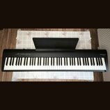 Černý digitální piano s bílými a černými klávesami a přiloženým notovým pultem. V pravém horním rohu je bílý nápis Roland FP30. V levé části horního…