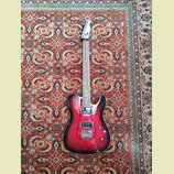 Elektrická kytara s červeným gradientem (sunburst) a viditelnou strukturou dřeva. Nástroj má dva humbuckery, jeden tónový potenciometr a jeden přepín…