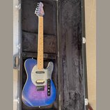 Modrá elektrická kytara typu Telecaster s javorovým hmatníkem v černém tvrdém kufru. Na korbisku je viditelné logo "Fender". Kytara má stříbrný plech…